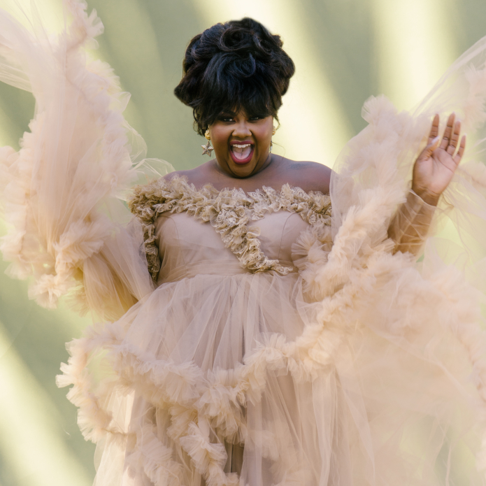 Nicole Byer smiles wide in a ruffly dusty rose dress.